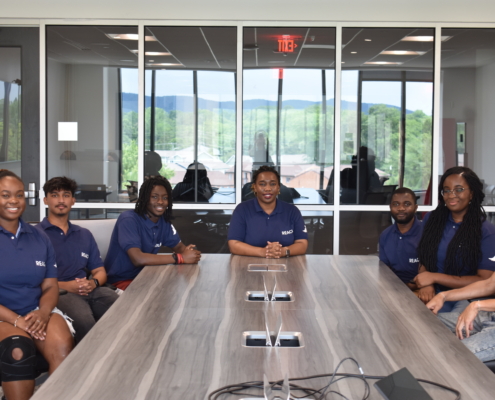 REACH Lab members sitting around a table in their blue lab shirts.